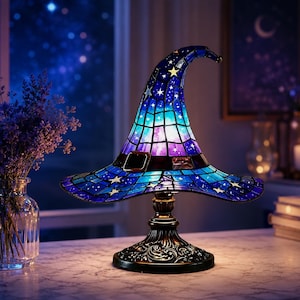 May include: A stained glass table lamp shaped like a pointed witch hat. The lamp features a gradient of blue, purple, and white glass panels decorated with small yellow stars and a dark band with a rectangular buckle around the base of the cone.