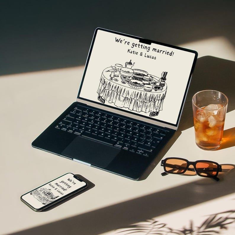 May include: A laptop computer with a black keyboard and a white screen displaying a hand-drawn illustration of a wedding reception table with the text "We're getting married! Katie & Lucas".