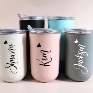 May include: Five insulated tumblers in white, black, pink, teal, and gray. Each tumbler has a lid and features a name in a cursive font with a heart symbol. The names are Shawna, Kim, and Jackson.
