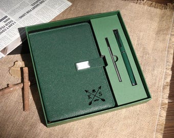 Puede incluir: Un juego de diario y bolígrafo de polipiel verde en una caja de regalo. El diario tiene un cierre plateado y un diseño en relieve con las iniciales "KS". El juego incluye un bolígrafo y un lápiz óptico.