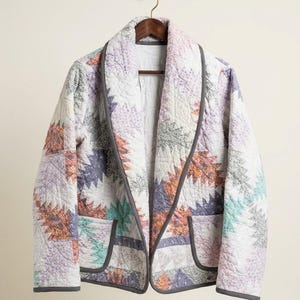 May include: A quilted jacket featuring a shawl collar and two front pockets. The garment is constructed from fabric panels in shades of lavender, peach, mint green, and white, all finished with a dark grey trim along the edges and seams.