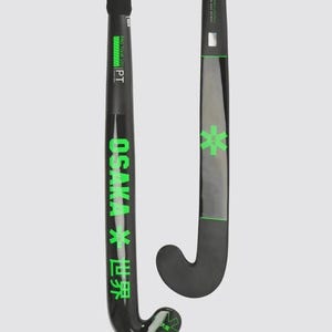Könnte beinhalten: Zwei schwarze Feldhockeyschläger mit neongrünen Akzenten. Die Schläger zeigen den Schriftzug OSAKA und japanische Schriftzeichen in Grün sowie ein grünes sternförmiges Logo. Die Griffe sind mit schwarzem Tape umwickelt und die Schäfte tragen das Pro Tour 100 Branding.