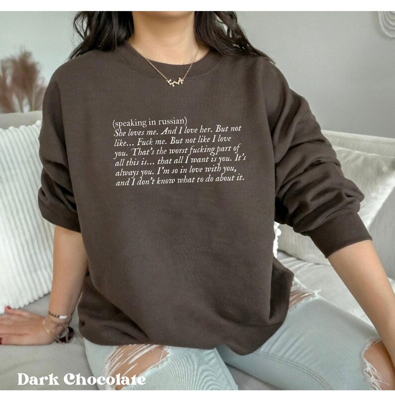 May include: Dark chocolate-colored sweatshirt with white text. The text includes a quote in English, beginning with "She loves me." The sweatshirt has long sleeves and a crew neck. The words "Dark Chocolate" are at the bottom.