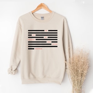 May include: A beige sweatshirt with the text "we are all immortal until proven otherwise" in a black and red design. The text is arranged in a rectangular block with horizontal black lines.