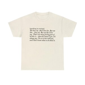 May include: Cream-colored t-shirt with black text. The text includes the phrase "She loves me. And I love her. But not like... Fuck me. But not like I love you." The shirt has a crew neck and short sleeves.