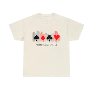 Puede incluir: Camiseta color crema con un dise&ntilde;o gr&aacute;fico que presenta los palos de las cartas y una silueta de paisaje urbano. El dise&ntilde;o incluye picas negras, diamantes rojos, tr&eacute;boles negros y un coraz&oacute;n rojo, con texto japon&eacute;s debajo.