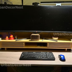 May include: A modern desk setup featuring a large curved monitor, a wooden monitor stand, and a black keyboard. The desk also includes a blue mouse, speakers, and decorative rubber ducks. The text "UrbanDecorNest" is visible.