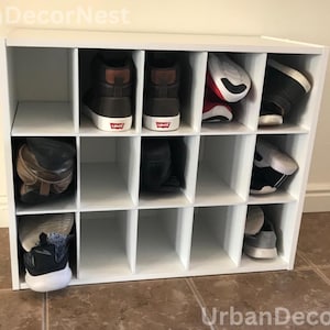 May include: A white shoe storage cabinet with multiple compartments, each holding a pair of shoes. The shoes vary in style and color, including sneakers, boots, and casual footwear. The cabinet is made of wood and is designed for home organization.