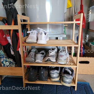 May include: A three-tiered bamboo shoe rack with multiple pairs of sneakers and shoes. To the left is a matching umbrella stand filled with umbrellas. The rack is made of light brown wood and sits on a blue mat.
