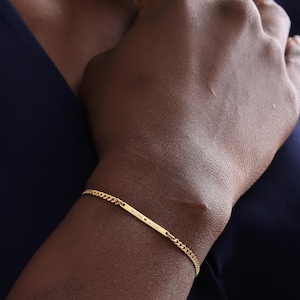 May include: A gold-colored bracelet with a rectangular bar and a chain-link design. The bar is engraved with the words "william & willow". The bracelet is worn on a wrist against a dark blue background.