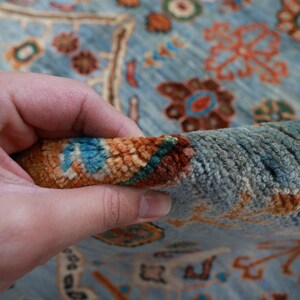May include: Close-up of a blue rug with intricate floral patterns in shades of orange, brown, and turquoise. The rug is made of a soft, plush material and has a hand-woven texture.