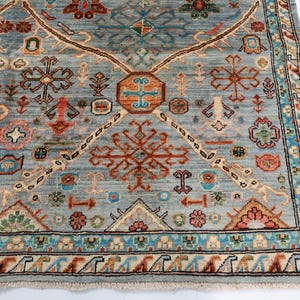 May include: A blue rug with a geometric pattern in shades of red, orange, and white. The rug has a fringe border.
