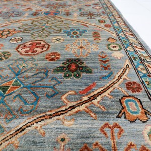 May include: A close-up of a blue rug with intricate patterns in shades of red, orange, green, and brown. The rug has a border with a floral design.