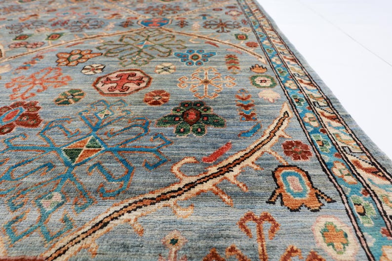 May include: A close-up of a blue rug with intricate patterns in shades of red, orange, green, and brown. The rug has a border with a floral design.