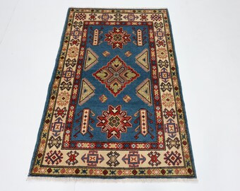 May include: A blue rug with a traditional geometric pattern in shades of red, cream, and brown. The rug has a fringe border.