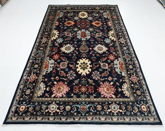 May include: A rectangular, navy blue area rug with an intricate floral pattern. The rug features a central design with cream, pink, and orange floral motifs, surrounded by a detailed border. The rug's design is symmetrical, with a traditional aesthetic.
