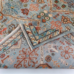 May include: A blue rug with a traditional Persian design. The rug has a detailed pattern with intricate floral and geometric motifs in shades of red, orange, and cream. The rug is folded in half, showing the fringe on the edges.