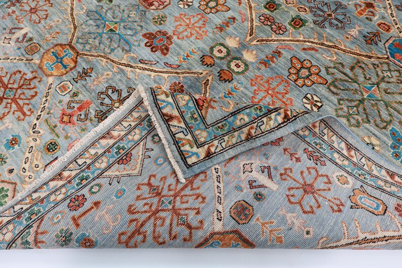 May include: A blue rug with a traditional Persian design. The rug has a detailed pattern with intricate floral and geometric motifs in shades of red, orange, and cream. The rug is folded in half, showing the fringe on the edges.