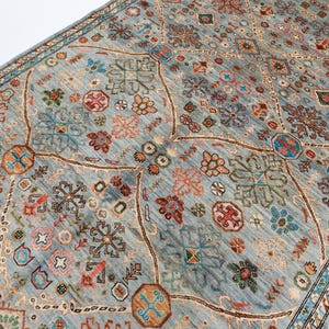 May include: A blue rug with a geometric pattern in shades of red, orange, green, and blue. The rug has a border with a repeating pattern.