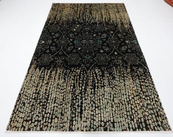 Puede incluir: Una alfombra rectangular negra con un patrón floral detallado en el centro y un diseño moteado en la parte inferior. La alfombra tiene un efecto degradado, que pasa de un beige moteado a un negro sólido.
