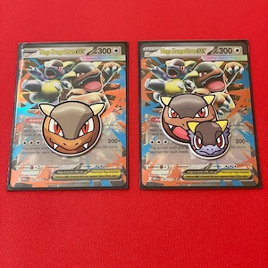 May include: Two Mega Kangaskhan EX Pokémon trading cards with matching character stickers. The cards feature a brown and tan kangaroo-like creature with a 300 attack power. The stickers are brown, tan, and yellow.