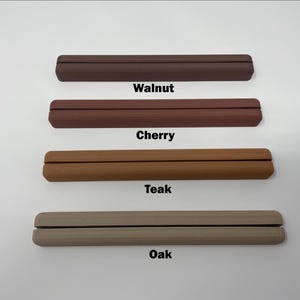 May include: Four wooden display stands in different wood finishes: walnut, cherry, teak, and oak. Each stand is a simple, rectangular shape with a groove in the center for holding items.