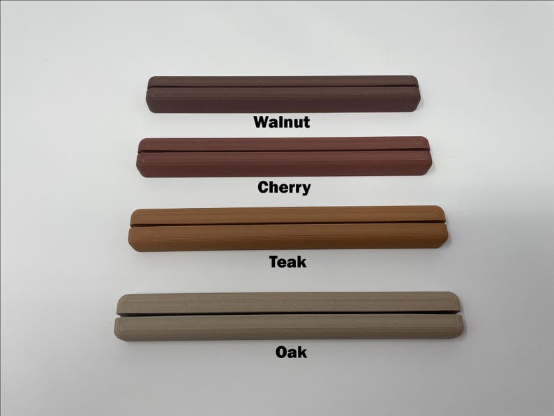 May include: Four wooden display stands in different wood finishes: walnut, cherry, teak, and oak. Each stand is a simple, rectangular shape with a groove in the center for holding items.