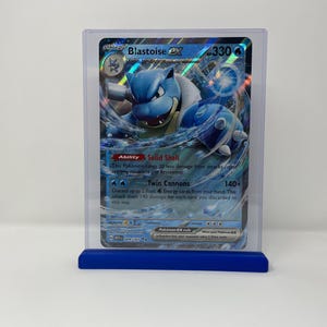 May include: A blue and white Pokemon card featuring Blastoise EX with the number 330. The card has an ability called Solid Shell and an attack called Twin Cannons.