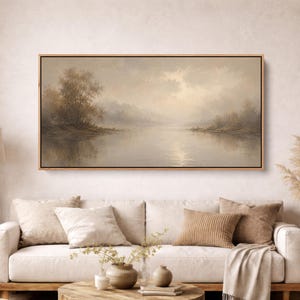 May include: A rectangular landscape painting in a wooden frame depicting a calm lake surrounded by trees under a soft, hazy sky. The artwork features muted earth tones, including beige, tan, and brown, capturing a serene, misty atmosphere.