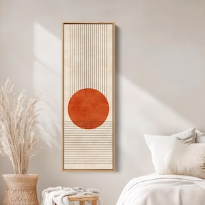 May include: Abstract wall art featuring a large orange circle over horizontal and vertical black lines. The artwork is set against a cream-colored background and framed in a natural wood tone. This piece is a modern, minimalist design.