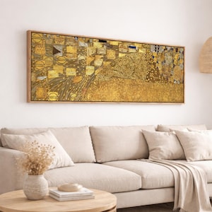 May include: A framed rectangular artwork with a gold and brown abstract design. The artwork features geometric shapes and patterns in shades of gold, brown, and black. The artwork is displayed above a beige sofa in a living room setting.