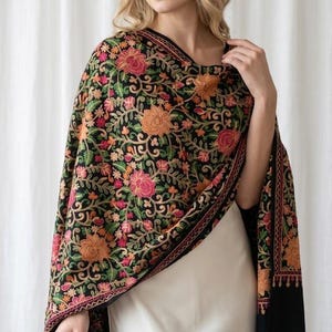 May include: A black shawl featuring intricate, multi-colored floral embroidery in shades of pink, orange, and green. The design covers the fabric with detailed botanical patterns, including large blossoms and winding vines, finished with a decorative border.