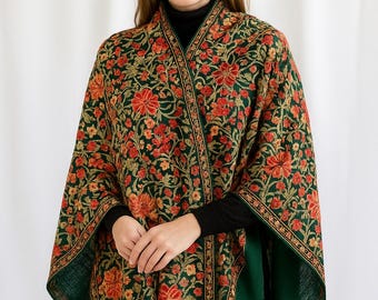 May include: A green shawl with a floral pattern in red, orange, and gold. The shawl is draped over the shoulders and has a dark green border. The woman is wearing a black turtleneck.