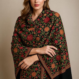 May include: A black shawl with a floral pattern in red, orange, and green. The shawl is draped over the shoulders and arms. The floral design is intricate and detailed, with a border of smaller floral patterns.