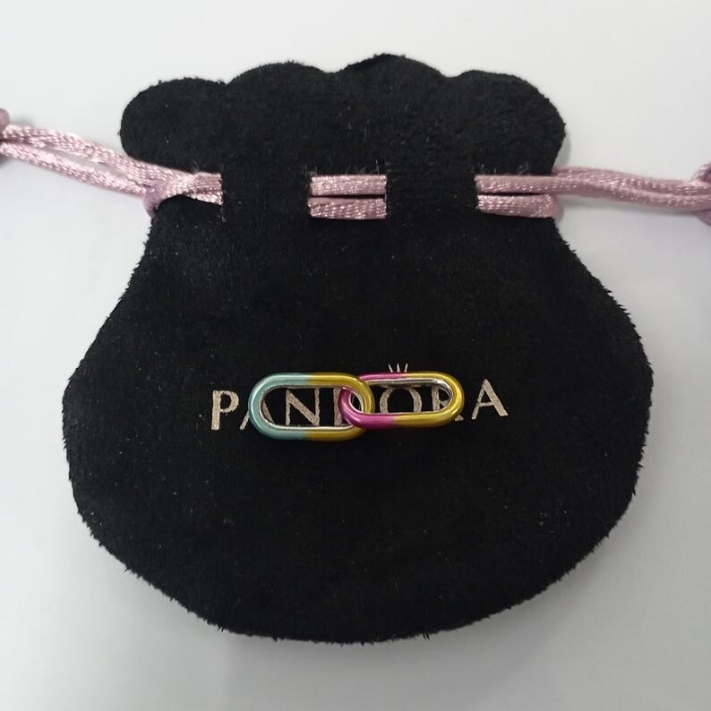 May include: A colorful Pandora charm in the shape of two connected links, with a gradient of blue, yellow, and pink. The charm rests on a black velvet pouch with the brand name printed in white.