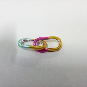 May include: Two linked oval-shaped silver links with a gradient color scheme. One link transitions from teal to yellow, while the other shifts from pink to yellow. The links are connected, creating a unique design.