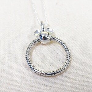 K&ouml;nnte beinhalten: Silberfarbene Halskette mit rundem Anh&auml;nger. Der Anh&auml;nger hat ein strukturiertes Design und einen kleinen herzf&ouml;rmigen Anh&auml;nger. Zwei abgerundete Akzente befinden sich oben. Die Kette ist filigran und silberfarben.