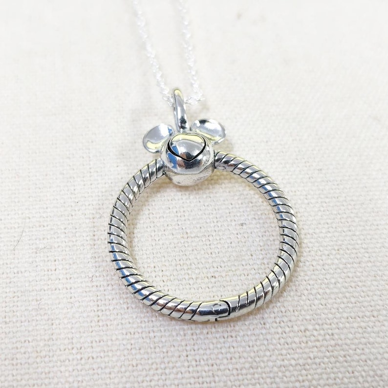 K&ouml;nnte beinhalten: Silberfarbene Halskette mit rundem Anh&auml;nger. Der Anh&auml;nger hat ein strukturiertes Design und einen kleinen herzf&ouml;rmigen Anh&auml;nger. Zwei abgerundete Akzente befinden sich oben. Die Kette ist filigran und silberfarben.