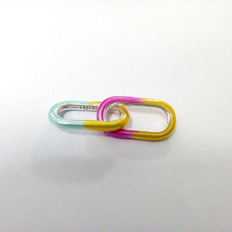May include: Two linked oval-shaped silver links with a gradient color scheme. One link transitions from teal to yellow, while the other fades from pink to yellow. The links are connected, creating a unique jewelry piece.