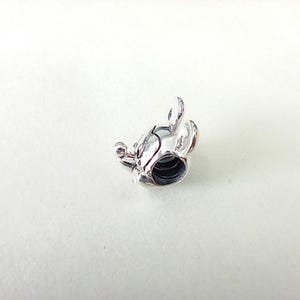 May include: A silver-colored charm in the shape of a mouse's head, featuring rounded ears, a small nose, and a circular opening. The charm is highly detailed and appears to be made of metal. The design is reminiscent of a popular cartoon character.