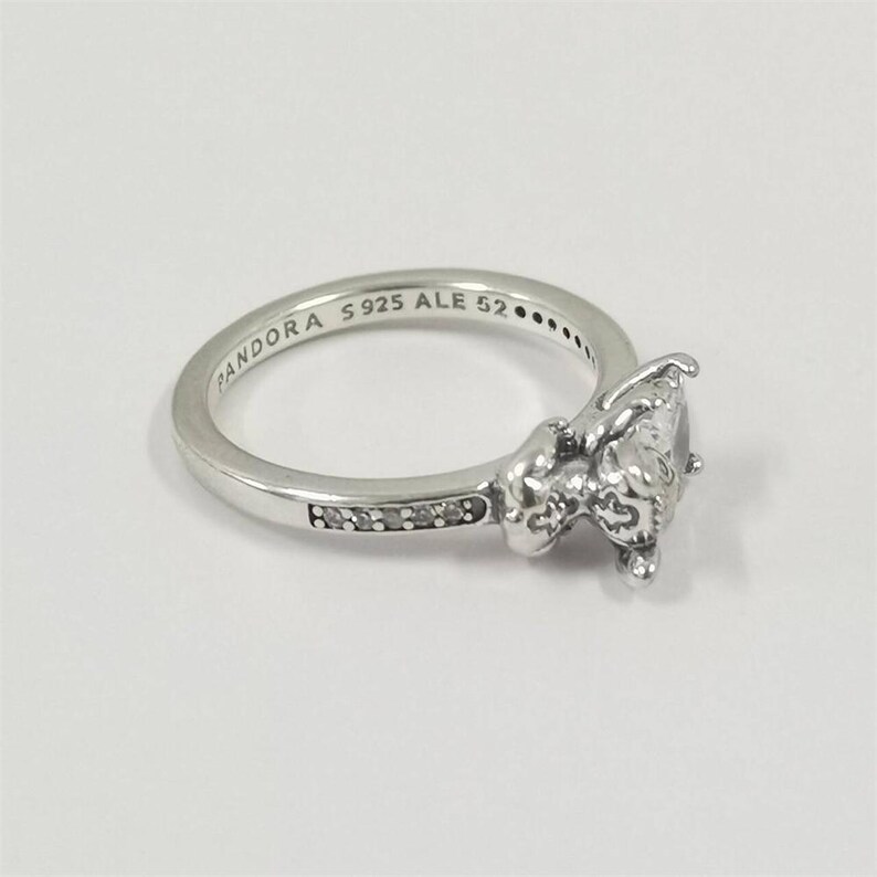 May include: A silver ring with a large, clear gemstone and smaller accent stones. The ring band is engraved with "PANDORA S925 ALE 52". The ring has a detailed, ornate design around the main gemstone, and is set against a white background.