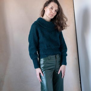 May include: A woman wearing a dark green fuzzy sweater and dark green leather pants.