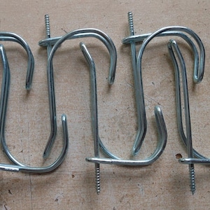 May include: Five silver metal hooks with screw-in bases. The hooks are designed for hanging items on a wall.