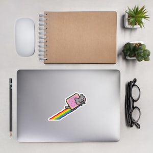 Puede incluir: Un gato pixelado gris que lleva un disfraz de tostada rosa y blanca corre sobre un arcoíris. El gato es un meme de internet popular.