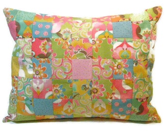 May include: A patchwork pillow with a rectangular shape. The pillow features a variety of colorful fabric squares in shades of pink, green, blue, and yellow. Floral and paisley patterns adorn the squares, creating a vibrant and decorative design.