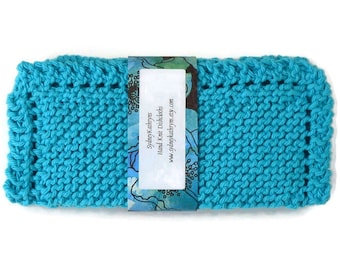 May include: A turquoise blue knitted dishcloth with a white border. The dishcloth has a label that reads "Sydney Kathryns Hand Knit Dishcloths www.sydneykathryns.etsy.com"