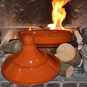 Peut inclure: Une tagine en terre cuite avec un couvercle. La marmite est posée sur un lit de bûches dans un foyer.