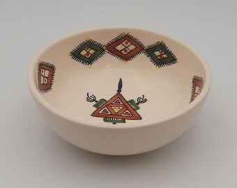 May include: A white ceramic bowl with a geometric design in shades of red, green, and yellow. The bowl has a triangular pattern in the center and a border of diamond shapes around the rim.