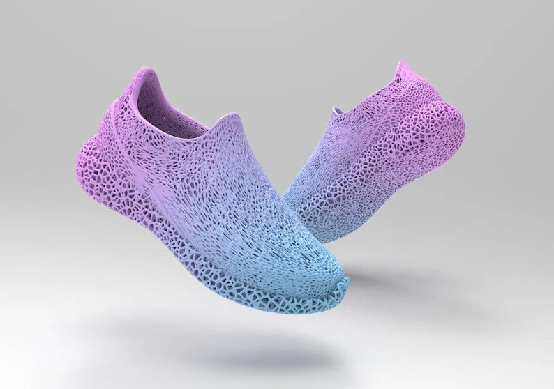 Puede incluir: Un par de zapatillas sin cordones en degradado azul y morado. Los zapatos tienen un dise&ntilde;o &uacute;nico de tejido abierto, creando una apariencia texturizada. Las zapatillas parecen flotar sobre un fondo blanco, mostrando su est&eacute;tica moderna.