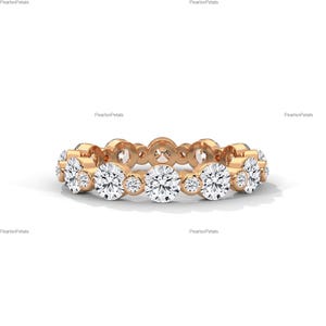 May include: A gold ring featuring a series of round, clear gemstones. The ring has a continuous design with larger stones alternating with smaller ones. The ring is set against a white background, highlighting its sparkle.